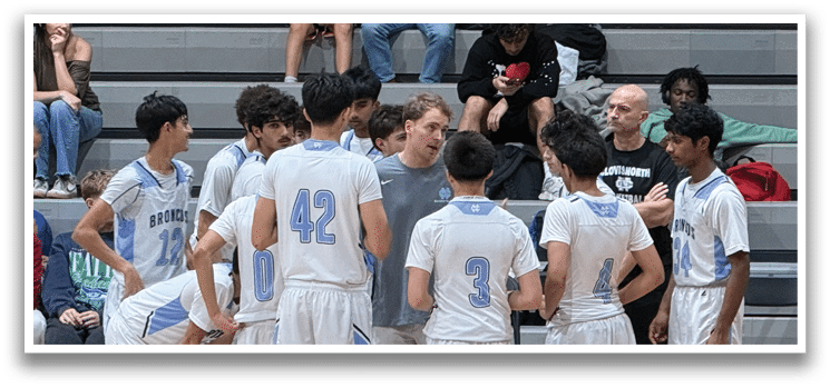 A group of young men are on a basketball court, some of them wearing blue shirts. They are gathered around a man who is talking to them. The men are standing in various positions, some closer to the man and others further away. There is a bench in the background, and a handbag can be seen placed nearby. AI generated content
