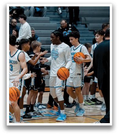 A group of young men and boys are playing basketball on a court. They are holding basketballs and shaking hands with each other. There are several people watching the game from the stands. AI generated content