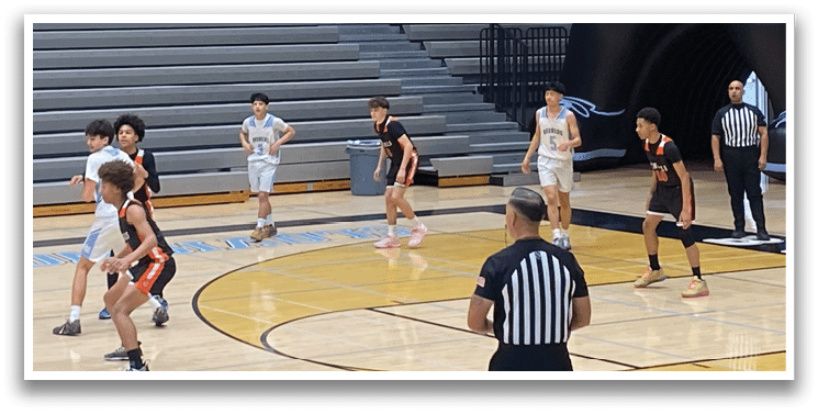 A basketball game is taking place in a gym with a crowd watching. The players are actively engaged in the game, with one player holding a basketball. A large inflatable bear is present in the gym, possibly as a mascot or decoration. AI generated content