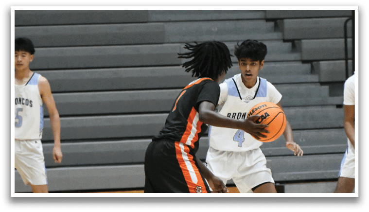 A basketball game is taking place with players on the court. One player is holding a basketball, while another player is trying to block him. The players are wearing uniforms and are actively engaged in the game. AI generated content