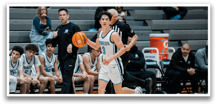 A basketball game is in progress with a player holding the ball. There are several people on the court, including players and a referee. Some players are sitting on chairs, while others are standing. A few people are also watching the game from the sidelines. AI generated content