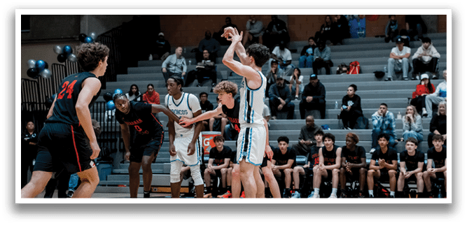 A basketball game is taking place with players on the court and spectators in the stands. A man is in the process of shooting a basketball, while other players are trying to defend. The game is being played in a gymnasium with a crowd of people watching the action. AI generated content