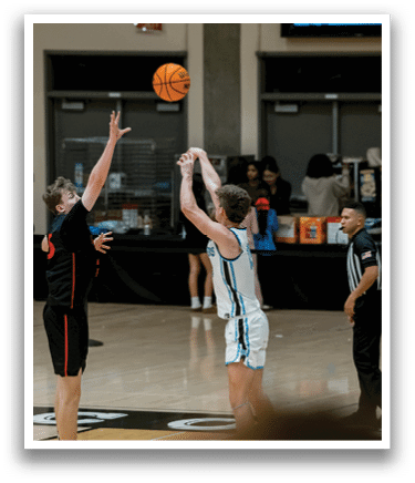 Two basketball players are reaching for the ball, both wearing black and white uniforms. The ball is in the air, and the players are trying to gain possession. There are other players on the court, some of them wearing red and white uniforms. A referee is also present, watching the game closely. AI generated content