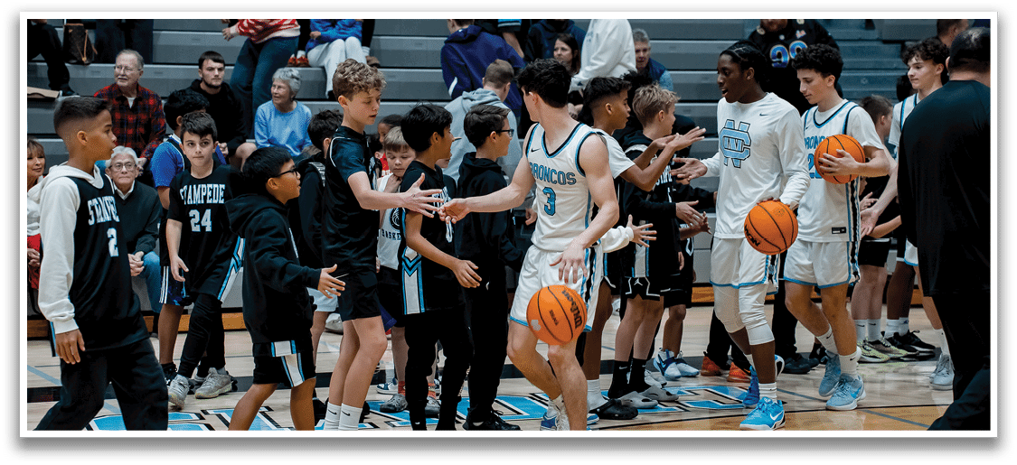 A group of young men and boys are playing basketball on a court. They are holding basketballs and shaking hands with each other. There are several people watching the game from the stands. AI generated content