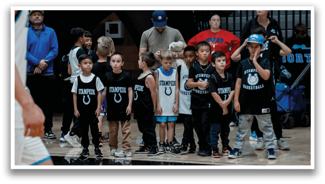 A group of children wearing sports jerseys are lined up on a basketball court, waiting for their turn to play. AI generated content