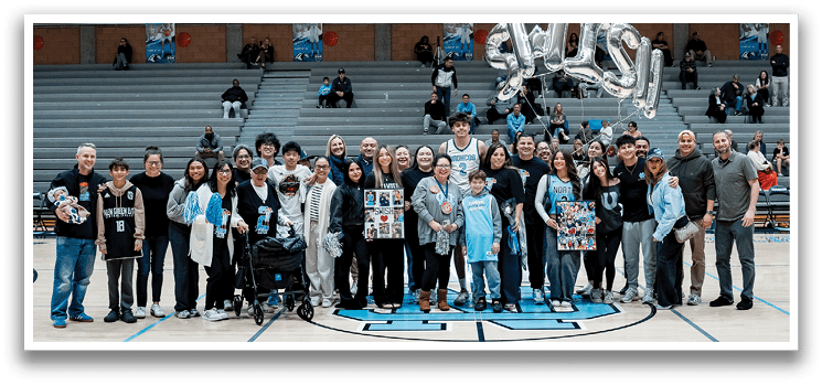 A group of people are standing on a basketball court, posing for a picture. They are holding balloons and some are wearing blue shirts. AI generated content