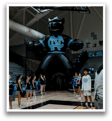 A group of cheerleaders are standing on a basketball court in front of a large inflatable mascot. AI generated content