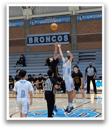 A basketball game is taking place in a gymnasium with a group of men playing. One man is attempting to shoot the ball while others are defending. The gym is filled with spectators watching the game. AI generated content