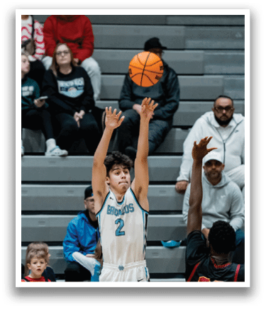A basketball game is taking place with two teams playing. One player is attempting to shoot the ball while others are watching. The audience is seated on chairs surrounding the court. AI generated content