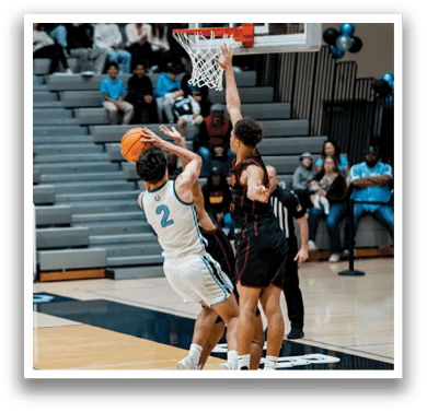 Two basketball players are leaping for the same ball, with one player wearing a blue shirt and the other wearing a red shirt. The players are in the middle of the court, surrounded by a crowd of spectators. AI generated content