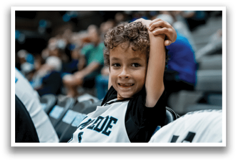 A young boy wearing a basketball jersey sits in the stands at a game. AI generated content