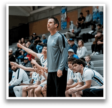 A man in a grey shirt stands on a basketball court, talking to a group of players. AI generated content