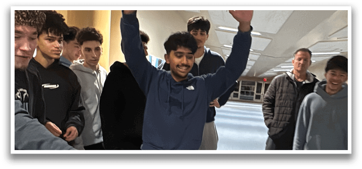 A group of young men are gathered around a table, with one of them raising his hand in the air. The others are watching and smiling, creating a friendly atmosphere. AI generated content