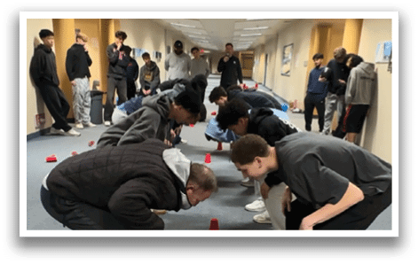 A group of people are playing a game in a hallway, with some of them bending over to pick up red cones. AI generated content