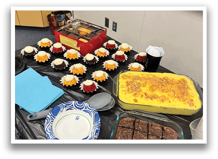 A table is filled with various desserts, including brownies, cupcakes, and a cake. There are also several plates and bowls containing different types of food. The table is set up for a gathering, with a black tablecloth covering it. AI generated content