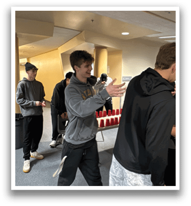 A group of young men are standing in a room, playing a video game. One of the men is holding a remote control, while another man is taking a picture of the gameplay. AI generated content