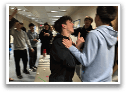 A group of people are playing a game in a room. One man is holding another man in a headlock while they both laugh. There are several other people in the room, some standing and some sitting. A dining table is visible in the room. AI generated content