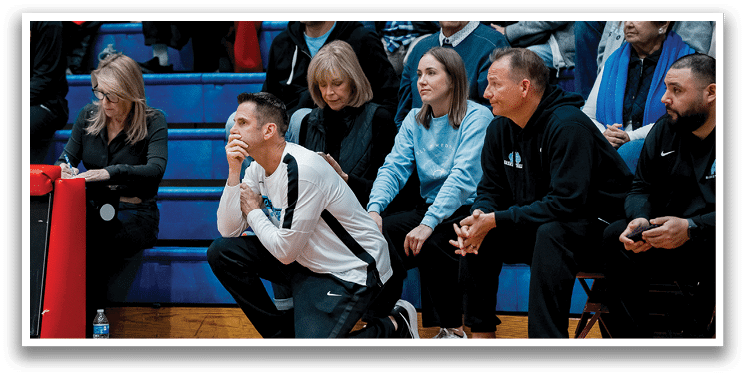 A group of people are sitting on a bench, watching a game. A man is kneeling on the ground, holding his head in his hands. AI generated content