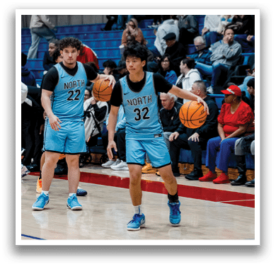 Two men wearing blue uniforms are playing basketball on a court. They are holding basketballs in their hands. There are several people watching the game from the sidelines. AI generated content