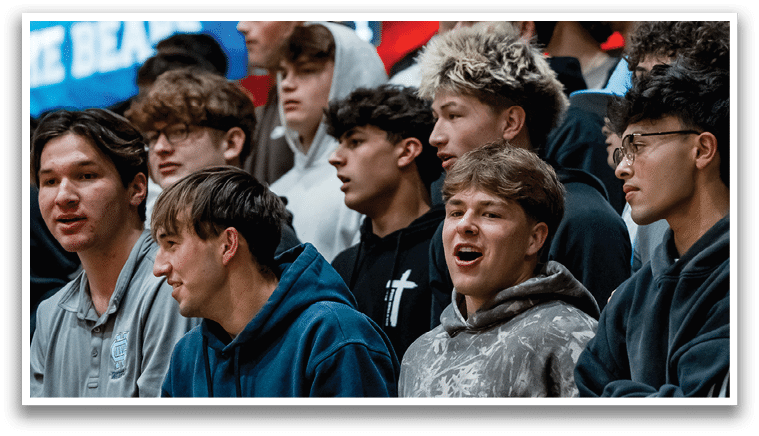 A group of people are sitting in the stands, watching a game. They are wearing various clothing, including hoodies and hats. Some of the people are wearing glasses. The crowd is engaged in the event and appears to be enjoying the game. AI generated content