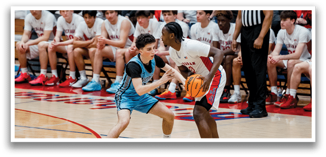 A basketball game is in progress with a group of young men playing. One player is holding a basketball while another player is trying to take it from him. The players are wearing uniforms and are surrounded by a crowd of spectators. AI generated content