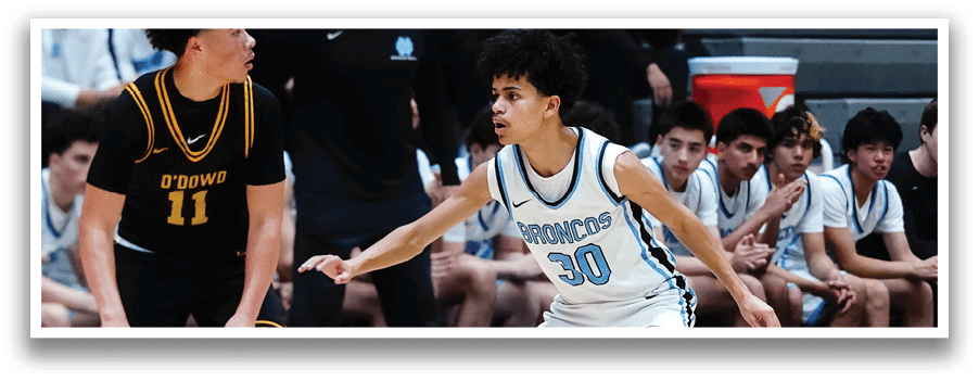 A basketball game is underway with players on the court. One player is holding a basketball while another player is trying to block him. The players are wearing uniforms and are in various positions on the court. There are also spectators watching the game. AI generated content