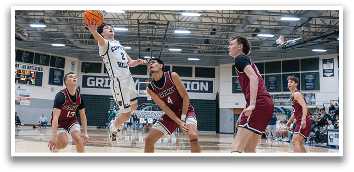 A basketball game is in progress with players on the court. One player is jumping to block a shot, while others are positioned around the court. The game is being played in a gymnasium. AI generated content