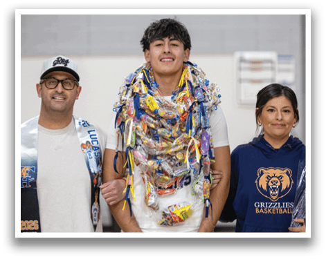 A man wearing a lei made of candy wrappers stands between two people, one of whom is holding a bouquet of flowers. AI generated content