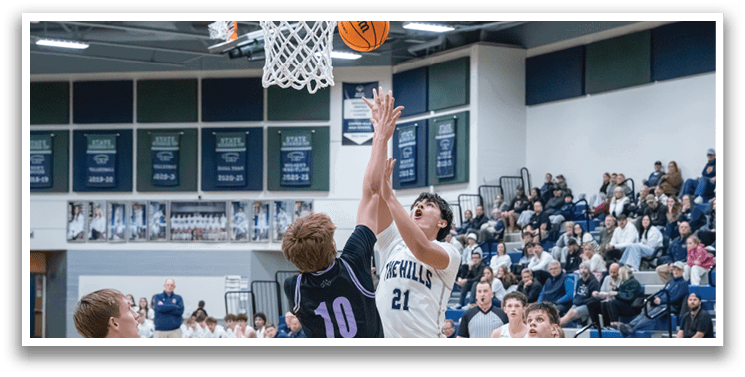 A basketball game is in progress with players on the court. One player is jumping to block a shot, while others are running and trying to get to the basket. The crowd is watching the game intently. AI generated content