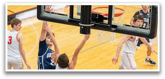 A basketball game is in progress with players on the court. One player is attempting to shoot the ball while another player tries to block the shot. The basketball is in the air, and the players are focused on the game. AI generated content