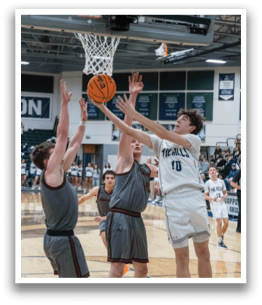 A basketball game is in progress with two teams playing. One player is jumping to block a shot, while another player is attempting to score. The crowd is watching the game intently. AI generated content