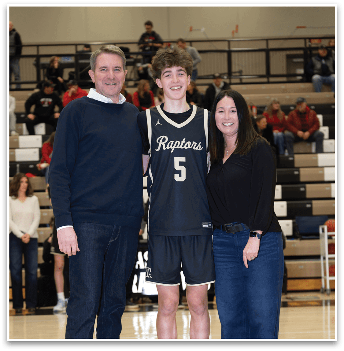 A man, woman, and boy pose for a photo on a basketball court. The man is wearing a black shirt and jeans, while the woman is wearing a black shirt and blue jeans. The boy is wearing a basketball uniform and holding a basketball. AI generated content