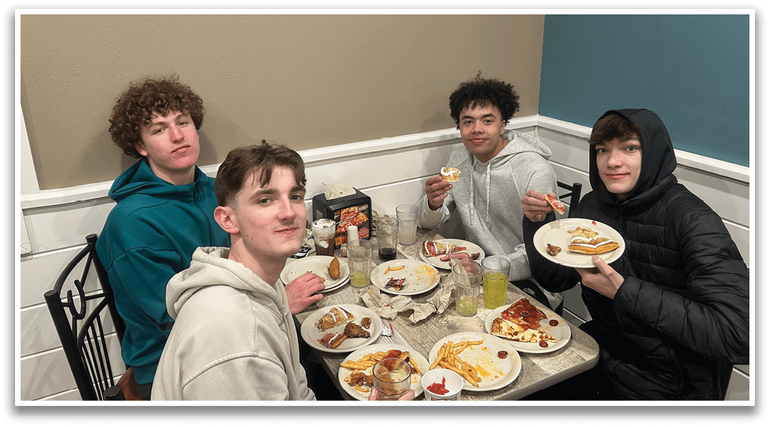 Four people are sitting around a table, enjoying a meal together. They are eating pizza and drinking soda. The table is set with plates, cups, and a bottle. The atmosphere appears to be casual and friendly. AI generated content