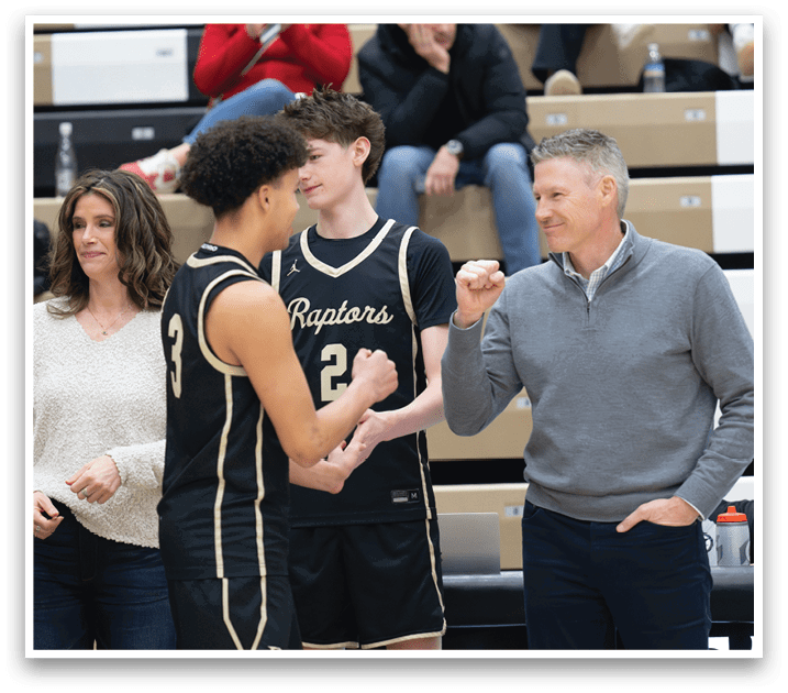 A group of people are sitting in the stands watching a basketball game. A man in a black and gold jersey is shaking hands with another man. The spectators are engaged in the game and watching the players. AI generated content