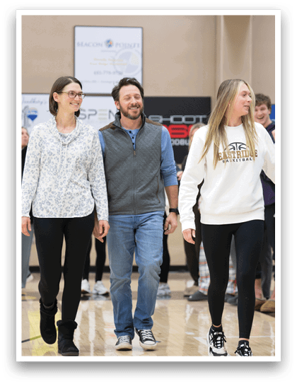 A group of people, including a man and a woman, are walking down a hallway. The woman is wearing a white shirt and black pants. The man is wearing a vest and jeans. The group is walking past a crowd of people who are watching them. AI generated content