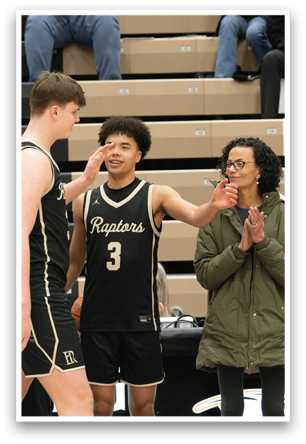 A group of people are standing on a basketball court, with one man holding up his hand to another man. A woman in a green jacket is clapping, and a man in a blue shirt is also clapping. The scene appears to be a celebration or recognition of the basketball player's achievements. AI generated content
