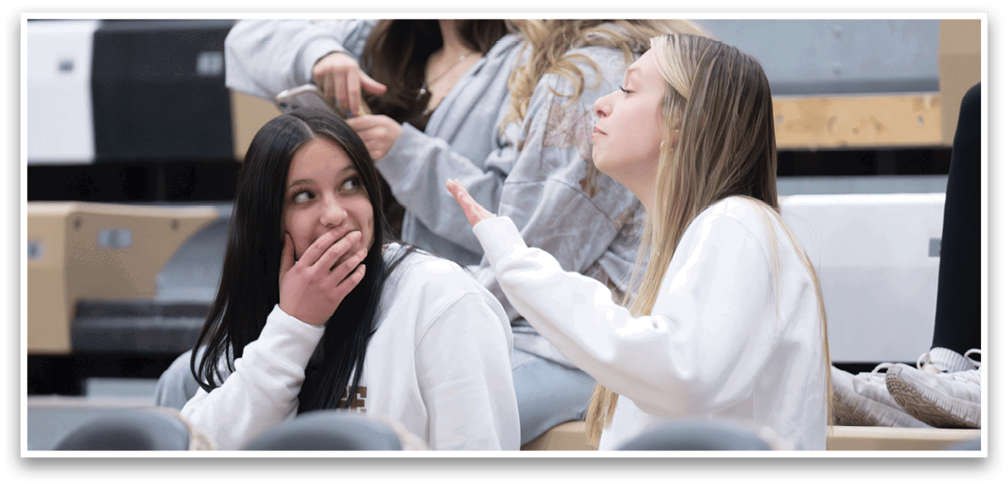 Three girls are sitting in a row, talking to each other. One girl is covering her mouth, while the other two are engaged in conversation. AI generated content