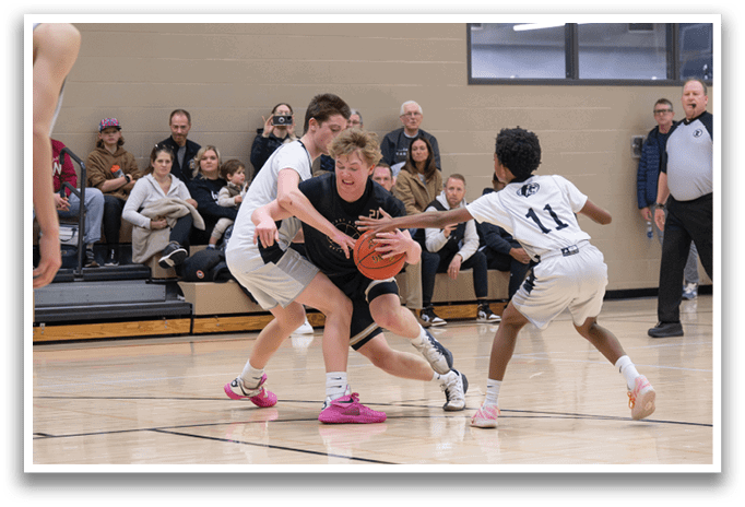 A group of people are playing basketball on a court. One player is attempting to steal the ball from another player. There are several other players on the court, some of whom are watching the action. A bench is located near the court, and a bottle can be seen on the ground. AI generated content