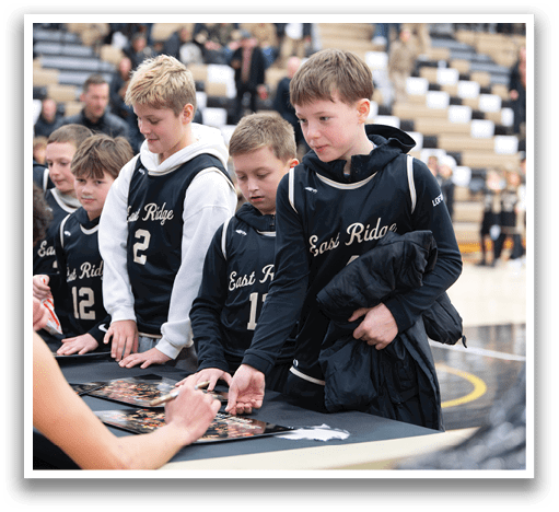 A group of young boys are gathered around a table, signing autographs for fans. AI generated content