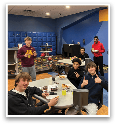 A group of young people are sitting at a table in a bowling alley, enjoying pizza and drinks. AI generated content
