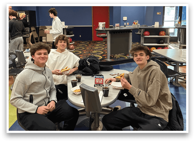 Three young men are sitting at a table in a bowling alley, enjoying pizza and drinks. AI generated content