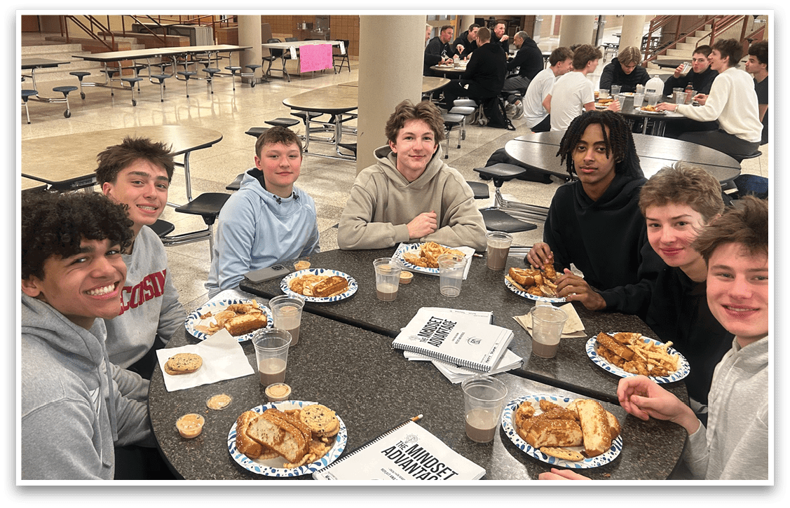 A group of young people are sitting around a table in a cafeteria, enjoying a meal together. AI generated content