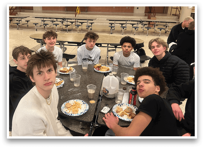 A group of young people are sitting around a table in a cafeteria, eating and drinking. AI generated content
