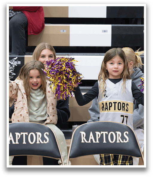 Two young girls are sitting in the stands, holding up cheerleader pom poms. They are wearing Raptors jerseys and are surrounded by other children. AI generated content
