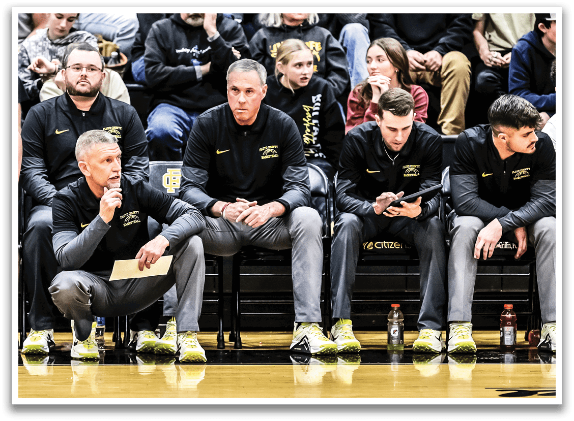 A group of men are sitting on a bench, some wearing sports uniforms. They are watching a game and holding water bottles. AI generated content