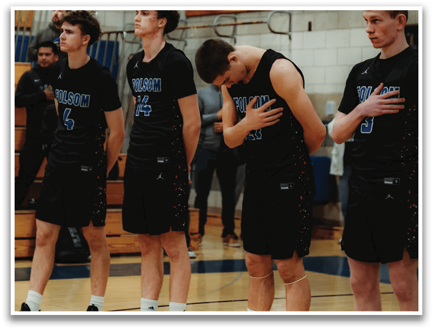 Four male basketball players are standing on the court, wearing black uniforms. They are lined up, with one player holding his head down. The players are standing in front of a crowd of spectators. AI generated content