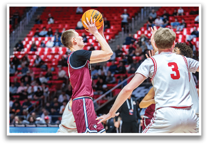 A basketball player in a maroon jersey shoots the ball while another player in a white jersey tries to block him. AI generated content