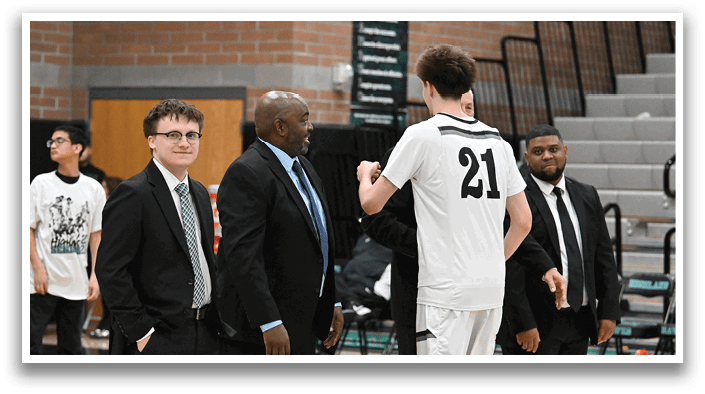 A group of men are standing on a basketball court, with one man wearing a white jersey and another man wearing a black suit. The man in the suit is shaking hands with the man in the white jersey. AI generated content