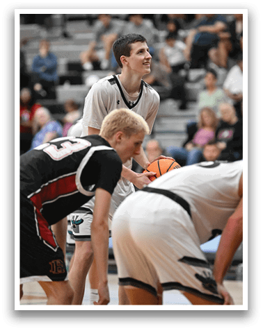 A basketball game is in progress with players on the court. A man in a white shirt is holding a basketball, while another player in a black shirt is looking on. There are several other players on the court, some of whom are wearing white shirts. The scene is filled with anticipation as the players prepare for the next play. AI generated content