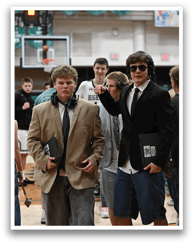 A group of people are standing in a gym, with some wearing suits and ties. A man in a suit is holding a microphone, and another man in a suit is holding a clipboard. A boy in a suit is giving a thumbs up. AI generated content